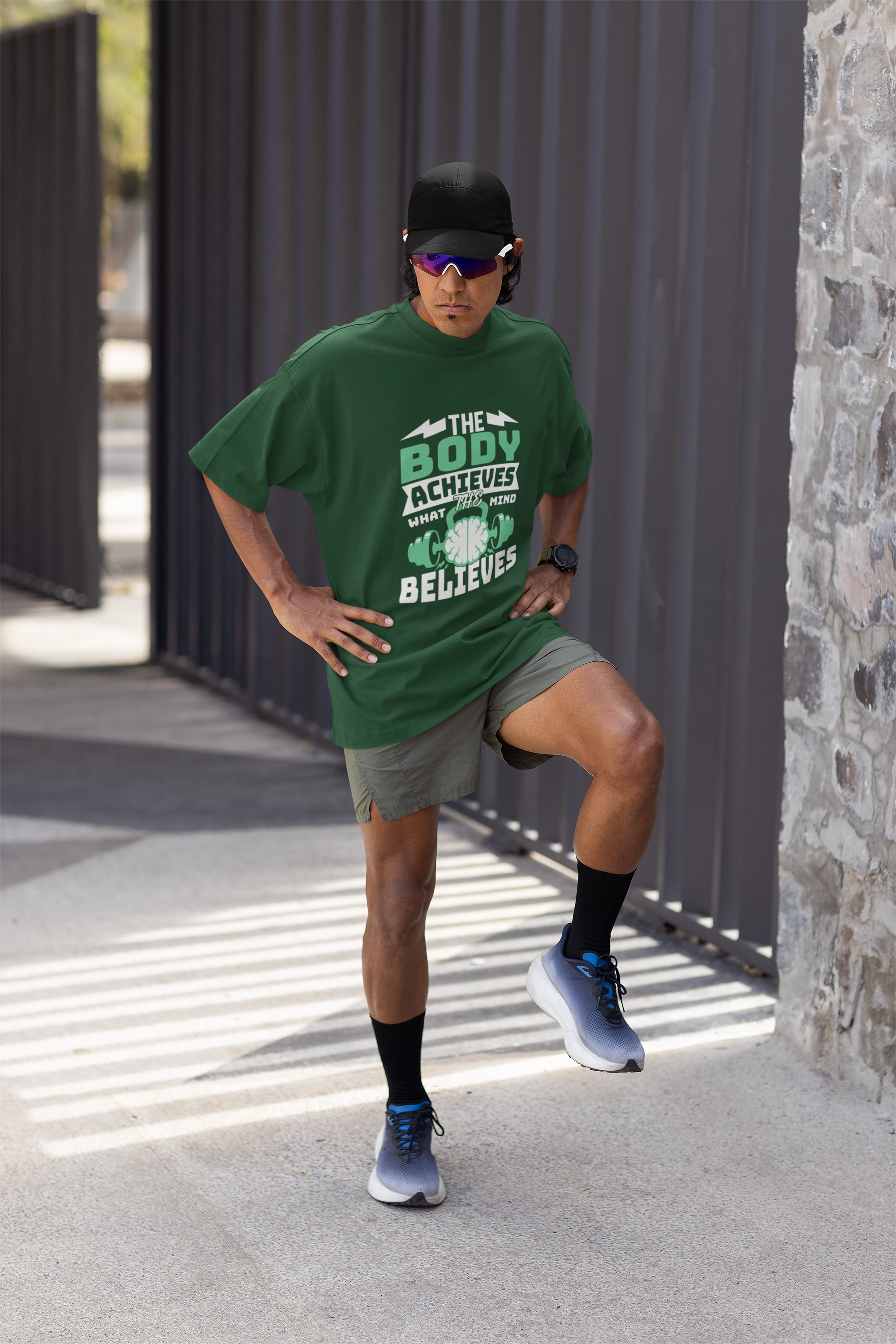 Person wearing a green t-shirt with text, gray shorts, and black socks on a beige background